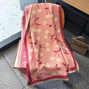 Detail of pink knitted scarf with white cherry patterns and fringe tassels on a wooden chair