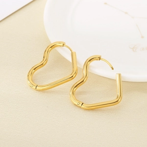Close-up of golden irregular heart-shaped hoops on a minimalist ceramic tray
