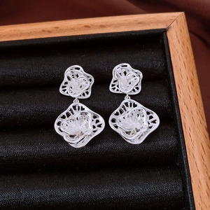 Detailed view of silver hollow flower dangle earrings on a premium black velvet tray