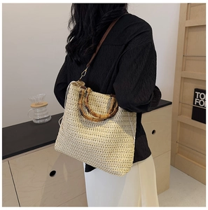 Detail of hand-woven straw beach bag with natural bamboo handle and brown strap