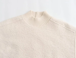 Detail of off-white knitted pullover showing plush texture and ribbed collar stitching
