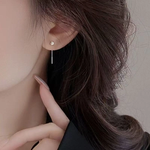 Macro detail of minimalist silver drop earrings showing sleek metallic texture on model's ear