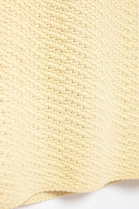 Macro detail of light yellow moss stitch knit fabric showing dense honeycombed texture