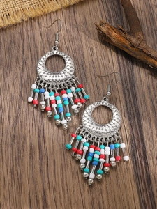 Detail of bohemian tassel earrings with carved metal rings and colorful beads on wood