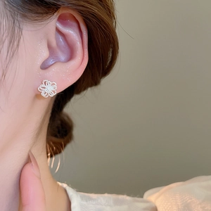 Close-up of minimalist hollow flower stud earring on ear with polished silver finish