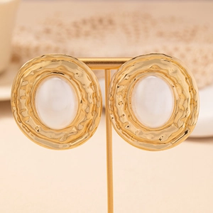 Close-up of golden geometric hoop earrings with hammered texture and white resin inlay