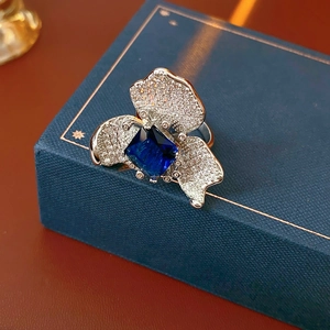 Macro detail of silver flower ring featuring deep blue square stone and pavé zircons