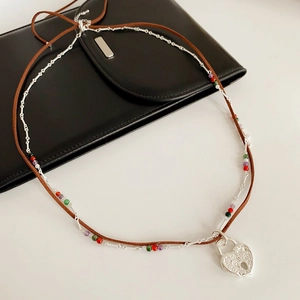 Close-up of double-layer brown leather cord and silver heart lock pendant necklace