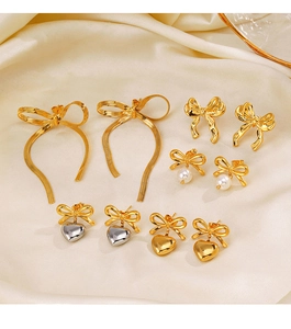 Vue à plat de boucles d'oreilles nœuds dorées avec perles et cœurs sur tissu en soie
