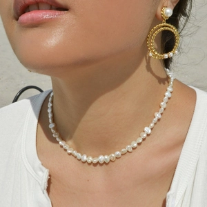 Detail of irregular freshwater pearl necklace and gold hoop earrings on model in sunlight