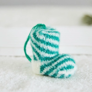 Green and white striped knitted Christmas boot ornament hanging on a snowy background