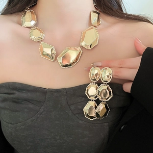 Gros plan d'un ensemble collier et boucles d'oreilles doré à facettes géométriques sur modèle
