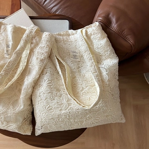 Detailed macro view of cream lace embroidery texture and fabric label on cotton tote bag