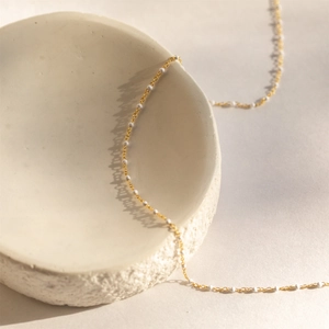 Detail shot of a bohemian golden chain necklace with white beads on a ceramic tray