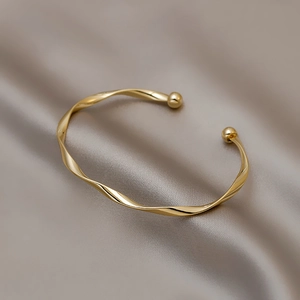 Bracciale rigido dorato a spirale minimalista con punte sferiche su seta elegante