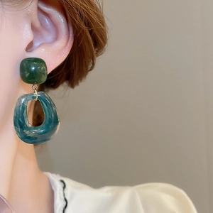 Close-up of geometric resin drop earrings with marble texture on model wearing white lace