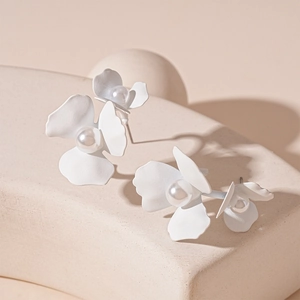 Detail showing white matte flower earrings with pearl centers on geometric props
