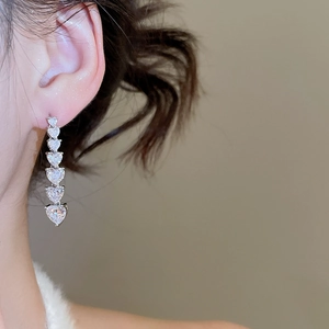 Detail of model wearing long silver heart earrings with gradient cubic zirconia stones