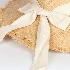 Macro shot of natural raffia sun hat texture with raw edges and a white fabric bow