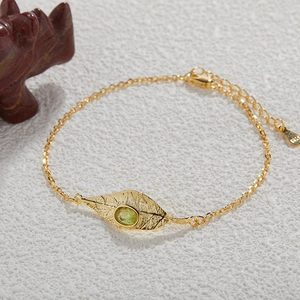Close-up of leaf charm with green gemstone and S925 silver stamp on gold chain