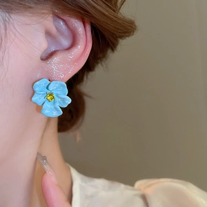 Detailed close-up of light blue floral stud earring with a yellow gemstone center