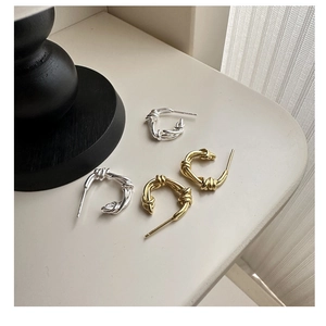 Close-up of knot design C-shaped earrings in polished gold and silver metallic finishes