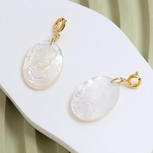 Macro view of oval white shell pendants with gold portrait relief and spring clasps