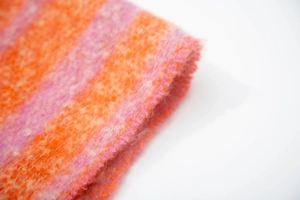 Macro detail of orange and pink striped bouclé knit scarf with fringe texture