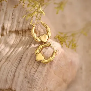 Detail view of 18K gold Claddagh hoop earrings with heart and crown on rustic wood
