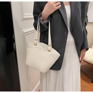 Close-up of a white pleated tote bag featuring golden metal rings and slim shoulder straps