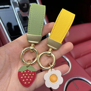 Premium leather car keychain with strawberry and daisy designs held in a luxury car interior