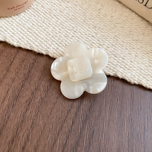 Detailed macro view of an ivory resin flower hair clip with marbled petals and text