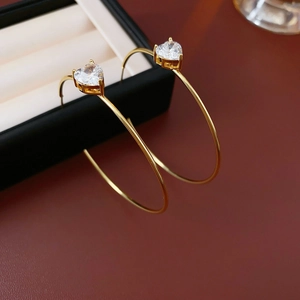 Détail macro de boucles d'oreilles créoles C dorées avec zircons étincelants en cœur