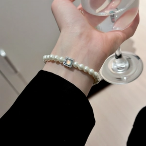 Detailed shot of pearl bracelet with blue gemstone charm worn on a female wrist
