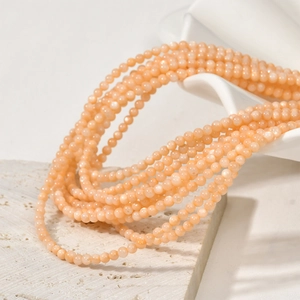 Macro detail of peach natural shell beads draped on white ceramic and stone base