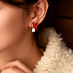 Détail de boucles d'oreilles papillon rouges dorées avec perles portées par un mannequin