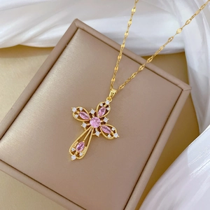 Detailed shot of a gold hollow cross necklace with pink and white gems on a silk box