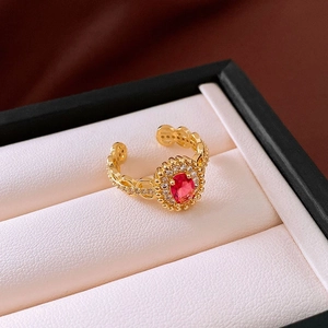 Detail of 18K gold-plated bow ring with ruby red gemstone in a beige jewelry box