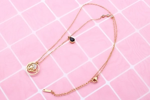 Close-up of gold double-layer necklace with Peace pendant and black gemstone drop detail