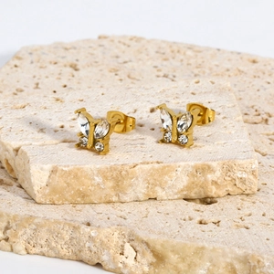 Close-up of gold butterfly stud earrings with clear rhinestones on a natural stone base
