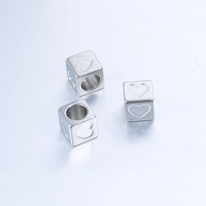 Macro shot of three silver 6mm stainless steel cube beads with engraved heart patterns