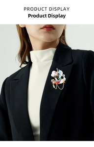 Detail of a gold-plated sailboat brooch with enamel moon and chain tassels on a blazer