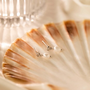 Detailed view of silver knot stud earrings with round white pearls on a shell