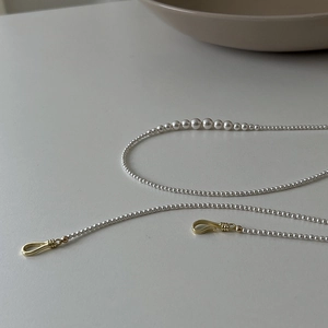 Close-up of elegant long pearl necklace with golden metal hooks on a minimalist white surface