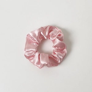 Close-up of pink satin scrunchie with soft silk texture and elegant pleated design