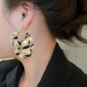Close-up of a model wearing large irregular golden earrings with a liquid metal texture