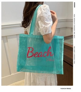 Detail of teal mesh beach bag with red Beach Vibes lettering on white lace dress
