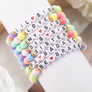 Close-up of pastel acrylic beaded bracelets with gold accents and Sister letter beads