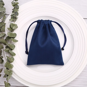 Detail of dark blue velvet jewelry pouch with drawstring on white ceramic plate