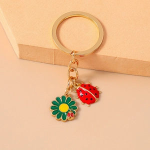 Macro detail of red ladybug and green flower enamel charms on a golden keychain